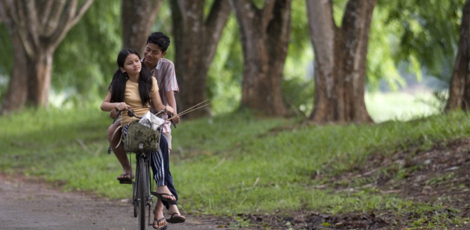 A girl and a boy ride a bicycle down a road - a still image from Mukhsin