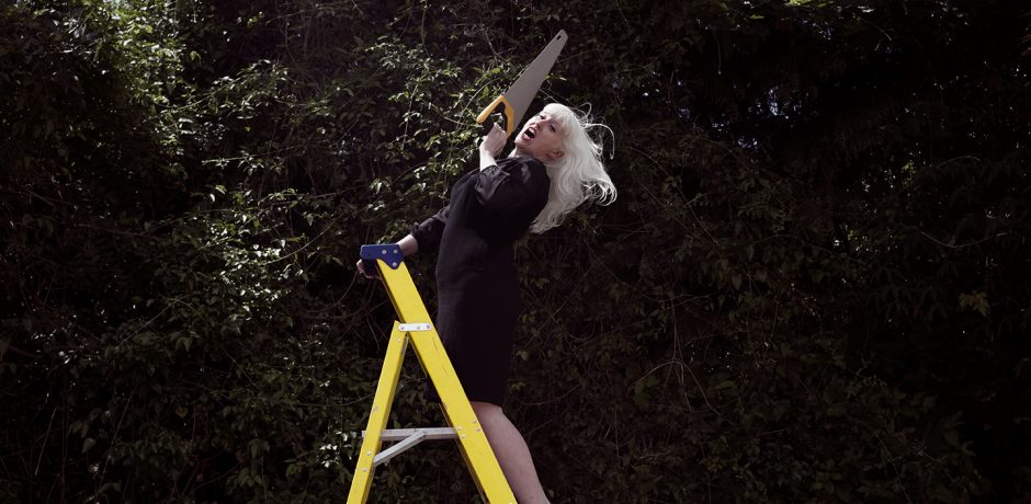 A woman standing on a ladder holds a saw