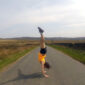 A woman performs a handstand on a deserted road, surrounded by hills. Lead image for Jenni Jackson's Endurance.
