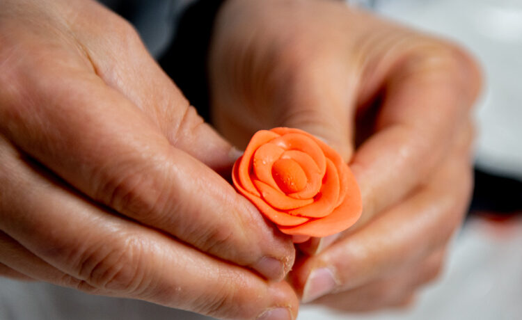 close up of a pair of hands holding a small, sculted orange flower made of wax