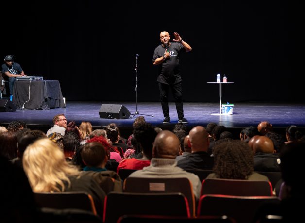 a comedian stand on HOME stage in front of audience.