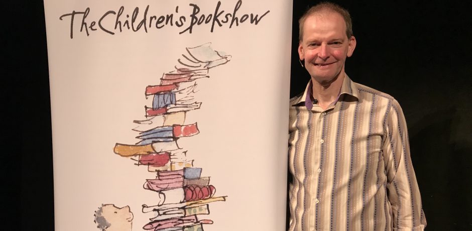 Author Daniel Morden stands next to a The Children's Bookshow banner
